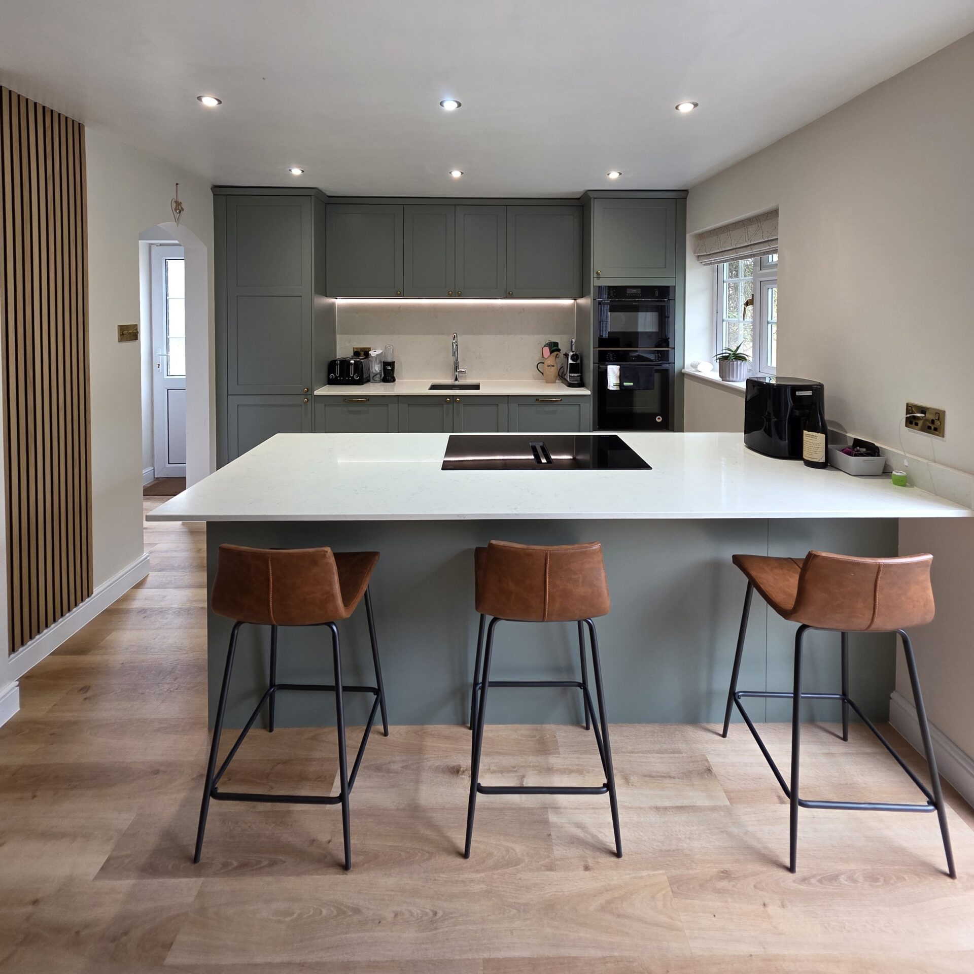 Sage green shaker kitchen with peninsula island with venting induction hob, light marble quartz worktops and barstools Sage green kitchen with Island